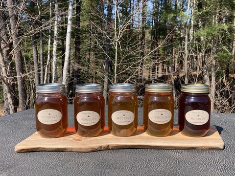 Five jars of maple syrup on a live-edge wood slab in front of the woodlot.