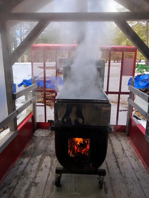 Inside the sugar shack, evaporator billowing steam over an open fire.
